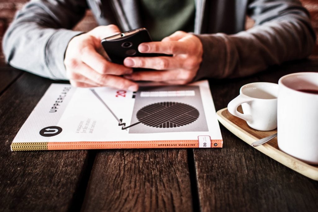 Person using phone with magazine and coffee